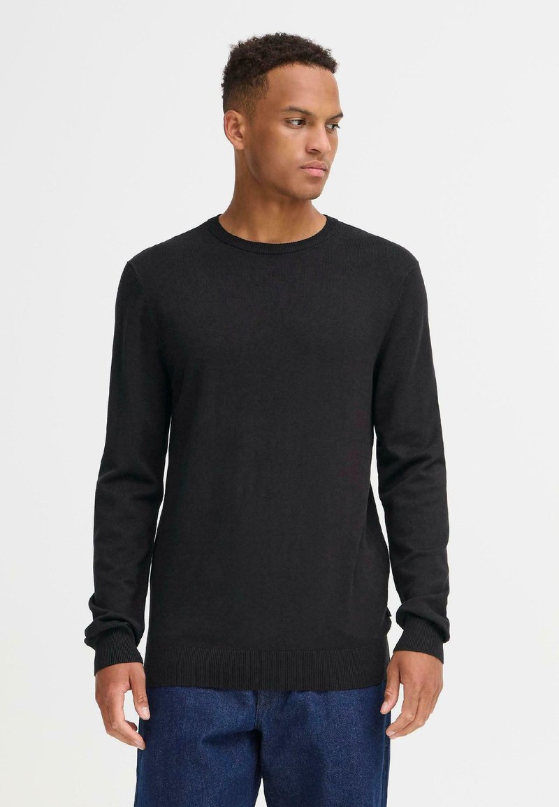 Suéter negro de manga larga con cuello redondo y puños y dobladillo acanalados. Hecho de tela texturizada, combinado con pantalones de mezclilla azul.