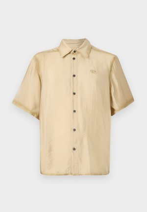 Rövid ujjú ing világos bézs selyemfényű anyagból, fényes felülettel, gombos elülső záródással és egy kis logóval a bal mellen.