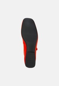 Suola della scarpa in gomma nera, con una superficie di presa testurizzata. Parte superiore in rosso brillante con finitura liscia e forma arrotondata.