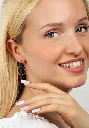 Silberne Creolen mit einer verlängerten ovalen Form, präsentiert an einem Modell mit langen blonden Haaren und hellrosa Nagellack.
