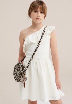 Jeune fille portant une robe blanche à volants, une épaule dégagée, et un sac bandoulière imprimé léopard avec un charm cœur.