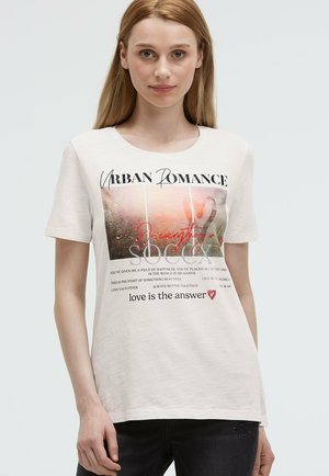 Light beige short-sleeve t-shirt featuring a graphic print with text, floral design, and red accents; made from a soft cotton blend.