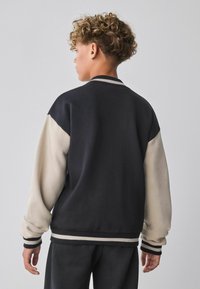 Sudadera negra y crema con mangas de contraste, puños y cuello acanalados. Tejido suave con un corte relajado.