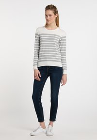 Pulover tricotat cu dungi gri și albe, cu gât rotund, asortat cu blugi skinny negri și adidași albi, pe un fundal simplu.