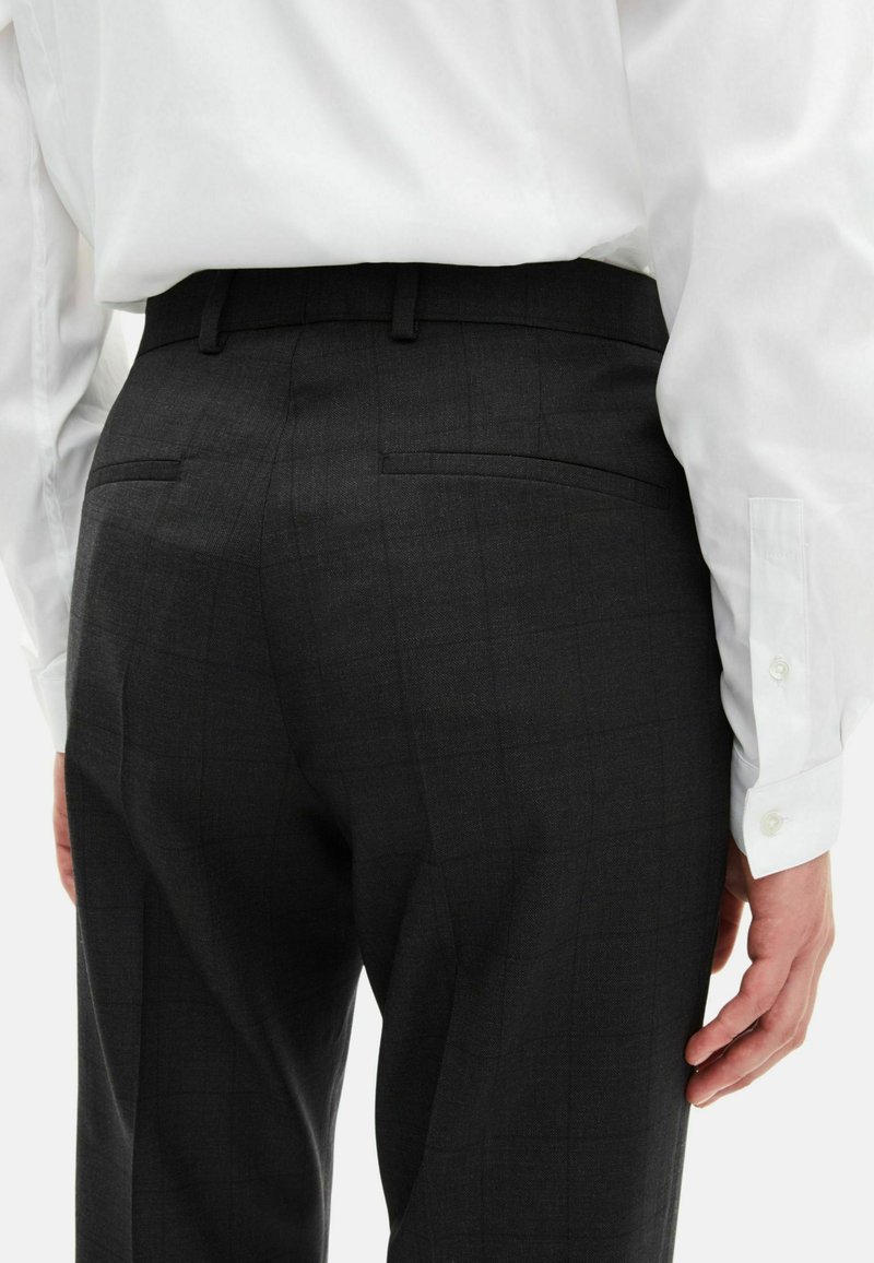 Donkergrijze broek met een subtiel ruitpatroon, voorzien van achterzakken en een getailleerde pasvorm, gecombineerd met een wit overhemd met knopen.