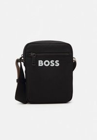 Melna taisnstūrveida somiņa pāri plecam no neilona. Tai ir priekšējā rāvējslēdzēja kabata un balts "BOSS" logotips. Regulējama siksna ar teksturētu detaļu.