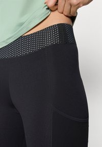 Black leggings with a textured, dotted waistband. The fabric is smooth and stretchy, with a side pocket and visible stitching details.