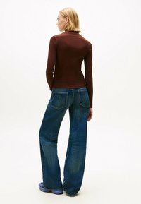 Top bordeaux a maniche lunghe abbinato a jeans blu larghi e strappati. L'outfit presenta una silhouette aderente e un tessuto testurizzato.
