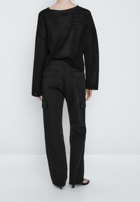 Musta neulepusero leveillä hihoilla, yhdistettynä mustiin cargo-housuihin, joissa on kaksi taka-taskua ja löysä istuvuus. Litteät mustat sandaalit.