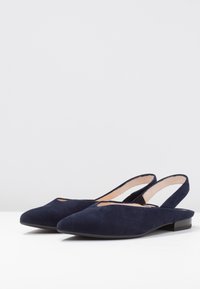 Mørkeblå ruskind slingback-sko med spids tå, flad sål og udskæring på vristen; har et minimalistisk design.