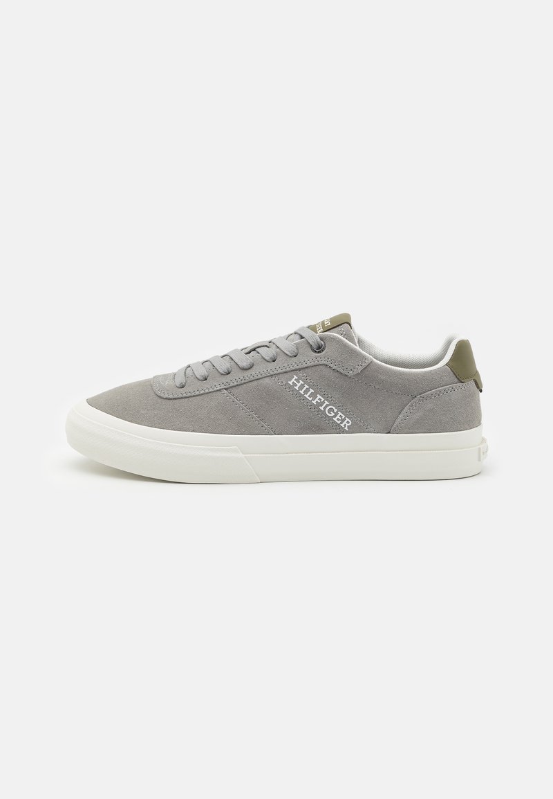 Baskets basses en daim gris avec semelle blanche, lacets, marquage "HILFIGER" sur le côté et détails vert olive au niveau du talon et de la languette.