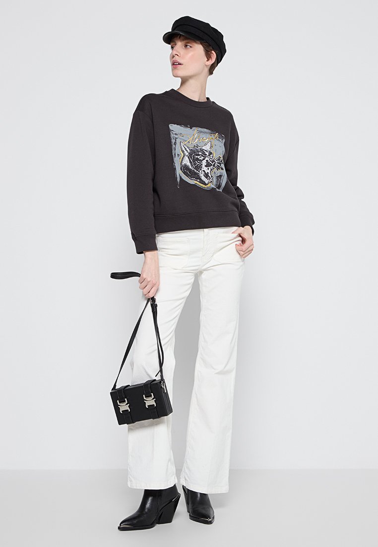 Schwarzer Pullover mit Grafik eines Wildkatze, kombiniert mit hoch taillierten, weißen Schlagjeans und schwarzen Ankle Boots. Schwarze Handtasche mit silberner Hardware.