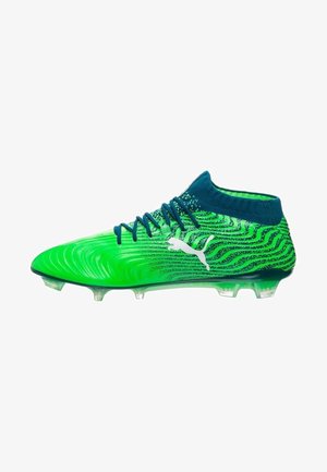 Bottines de football vertes et bleues avec un dessus texturé, présentant un motif en vagues et une semelle transparente. Comprend des lacets bleu foncé et un col de cheville.