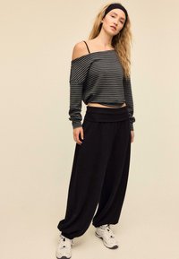 Črne široke hlače z visokim pasom, kombinirane z ohlapno črno-sivo črtasto bluzo z razkritimi rameny. Bele športne superge.