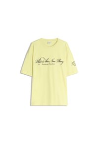 T-shirt din bumbac galben cu o croială lejeră. Are textul "Asta este Noua Lucru" în cursiv negru și detalii cu logo pe mânecă.