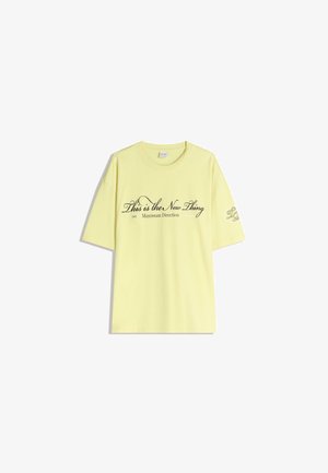 T-shirt in cotone giallo con vestibilità rilassata. Presenta il testo "Questo è il nuovo trend" in corsivo nero e un dettaglio del logo sulla manica.