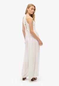 Abito maxi bianco con corpino aderente, schiena scoperta con spalline e gonna fluttuante. Tessuto leggero e liscio con una sottile trama.