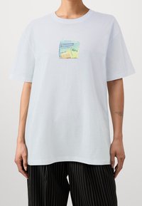 Valkoinen puuvillainen t-paita, jossa edessä värikäs mehutetrin kuvio. Lyhyet hihat ja rento istuvuus. Näkyvissä raidalliset housut.