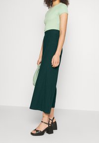 Ciemnozielone spodnie szerokie z bocznym rozcięciem, w połączeniu z jasnoniebieską dopasowaną koszulką. Czarne platformy na obcasie z paskami na kostkach. Mała zielona torebka.