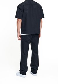 Camisa negra de manga corta con corte recto, combinada con pantalones negros. El calzado son zapatillas blancas. La tela parece duradera y texturizada.