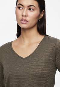 Oliven grønn V-hals topp med subtilt gull horisontalt stripe mønster, laget av et lett, teksturert stoff. Har en tettsittende design.