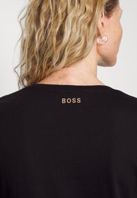 Black t-shirt with a round neckline and short sleeves. Features a subtle gold "BOSS" logo on the upper back. Smooth, lightweight fabric.