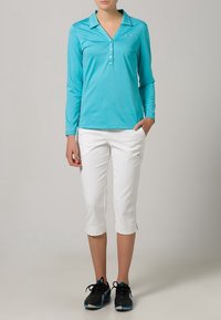 Långärmad turkosskjorta med krage och knappar, i kombination med vita capribyxor. Svarta löparskor med blå detaljer.