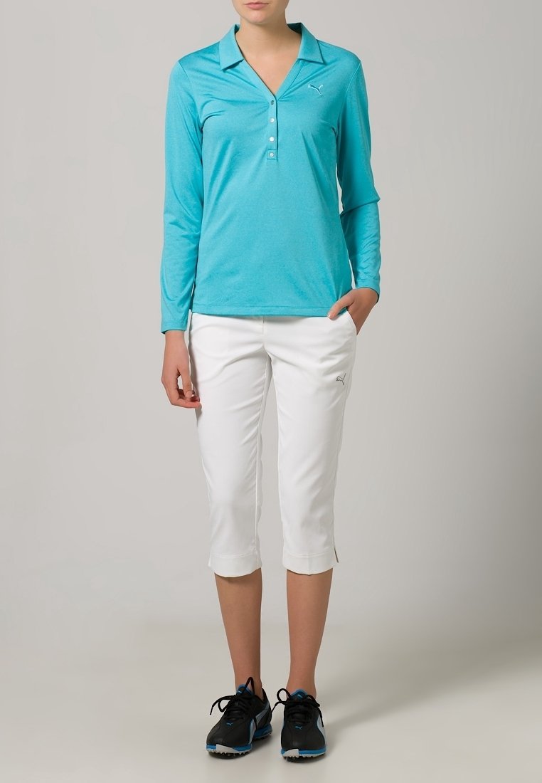Långärmad turkosskjorta med krage och knappar, i kombination med vita capribyxor. Svarta löparskor med blå detaljer.