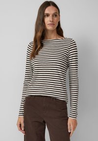 Gestreepte langekleurige top in crème en bruin, met een brede halslijn en aansluitende mouwen. Draagt met een donkerbruine broek.