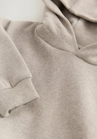 Felpa grigia in cotone caratterizzata da una texture morbida, tasca a marsupio, polsini a costine e cappuccio con coulisse. Inquadratura ravvicinata che mette in evidenza i dettagli del materiale.