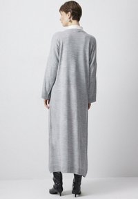 Cardigan lung gri cu un model texturat în dungi, cu spatele deschis și mâneci largi. Asortat cu cizme negre până la genunchi.