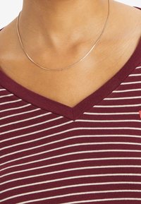 Burgundy v-neck top with white horizontal stripes, made of soft fabric, features a ribbed neckline and a fitted design. Silver chain necklace included.