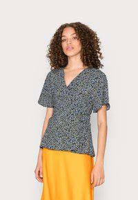 Topo floral envolvente em azul escuro com padrões amarelos e brancos, mangas curtas e cintura ajustada. Combina com uma saia amarela brilhante.