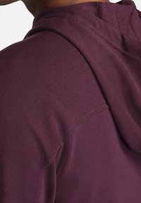 Sweat à capuche bordeaux avec une texture lisse et une capuche à cordon. Présente des détails de couture subtils, mettant en valeur une coupe ajustée et un tissu respirant.