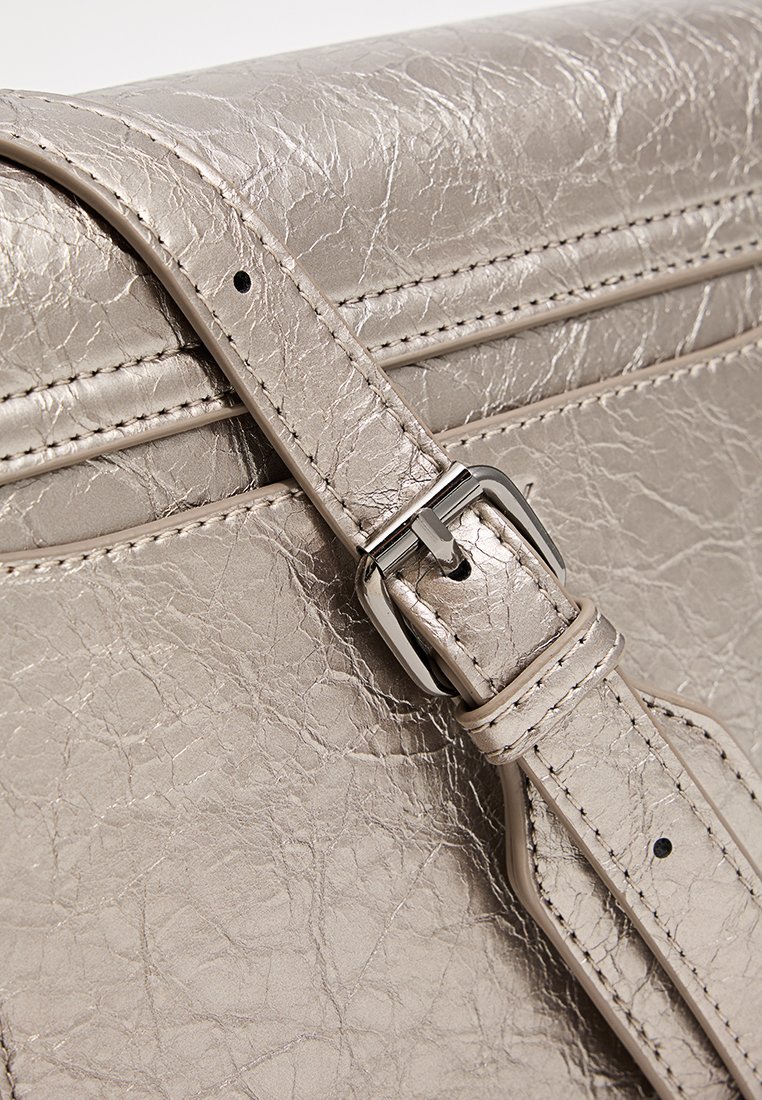 Metallisch silberner Handtaschenriemen mit einer strukturierten Lederoberfläche, ausgestattet mit einer silberfarbenen Schnalle und Nähdetails.