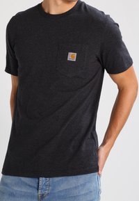 T-shirt corto a maniche corte di colore grigio scuro, realizzato in cotone, con una tasca sul petto decorata da un logo arancione quadrato. Vestibilità classica con scollatura a girocollo.