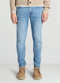 Jean en denim bleu clair à coupe slim, avec des détails délavés et un design à cinq poches, associé à des chaussures en daim couleur beige.