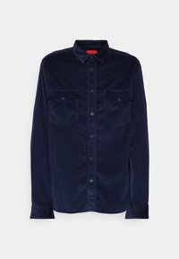 Chemise en velours côtelé bleu marine à manches longues, boutonnée sur le devant avec deux poches poitrine à rabats sur fond uni.