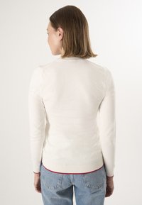 Crème-kleurige trui met lange mouwen, geribbelde halslijn en manchetten, met een rode accent aan de onderkant. Soepele textuur, getailleerd ontwerp.
