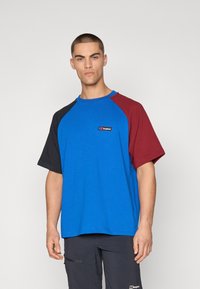 Color-blocked short-sleeve t-shirt featuring blue, black, and burgundy panels. Soft cotton material with a round neckline and logo detail.