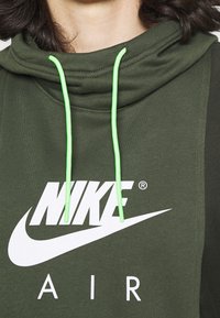 Felpa verde con cappuccio alto, caratterizzata da logo Nike bianco e scritta "AIR". I cordini sono di colore verde neon. Tessuto strutturato, vestibilità casual.