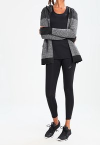 Sort atletisk tanktop kombineret med en grå, letvægtshættejakke med en teksturblanding. Sorte leggings og sorte sneakers fuldender outfittet.