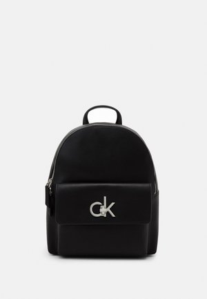 Schwarzer Mini-Rucksack aus Leder mit Frontklappentasche, silbernem CK-Logo, oberem Tragegriff und Reißverschluss auf schlichtem weißem Hintergrund.