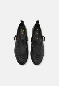 Zapatos estilo Mary Jane perforados en negro, con punta redondeada, correa ajustable y hebilla en tono dorado. Fabricados en material sintético suave.