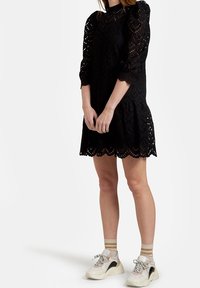 Svart spetklänning med långa puffärmar, vågig nederkant och utskärningsmönster. Kombinerad med beige och vita sneakers.