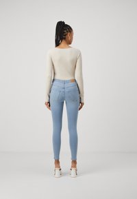 Jeans skinny de azul claro com uma cintura alta, complementados por uma blusa de manga longa canelada creme e sapatos brancos de salto bloco. Design minimalista.