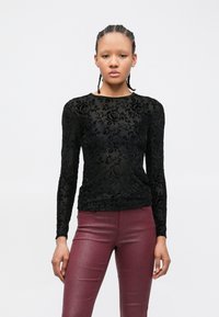 Schwarzes Langarmshirt mit floraler Spitzenmusterung, ausgestattet mit rundem Ausschnitt und schlanker Passform, kombiniert mit glänzenden burgunderroten Hosen.