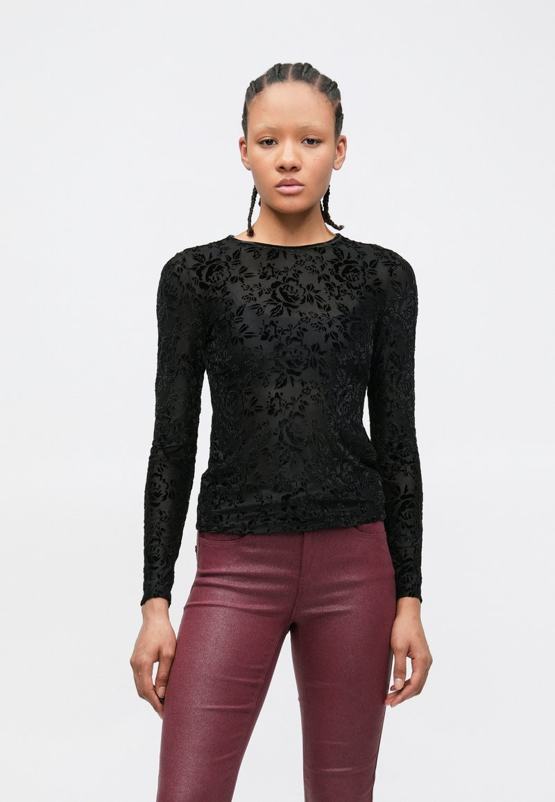 Schwarzes Langarmshirt mit floraler Spitzenmusterung, ausgestattet mit rundem Ausschnitt und schlanker Passform, kombiniert mit glänzenden burgunderroten Hosen.