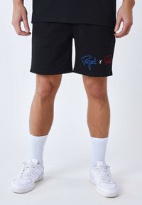 Shorts noirs en coton, ornés du texte brodé bleu et rouge "Project x Paris" sur le bas à gauche. Assortis à des chaussettes blanches et des baskets.