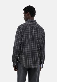 Chemise à carreaux noir et blanc en tissu texturé, avec un col boutonné et des manches longues, vue de dos.